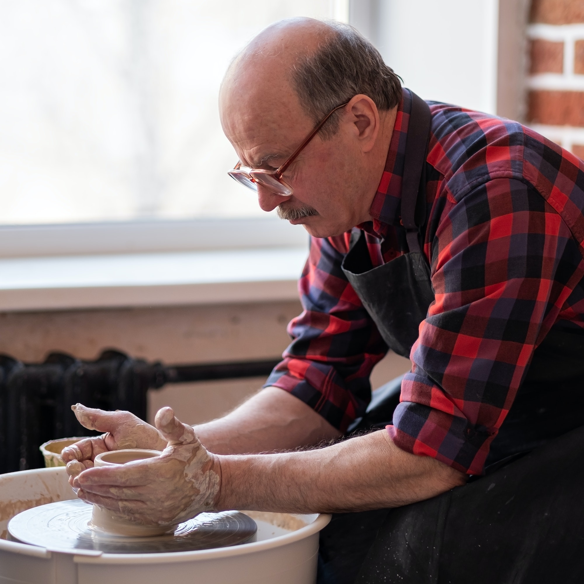Senior male potter creating bowl in pottery workshop. Hobby at old age.