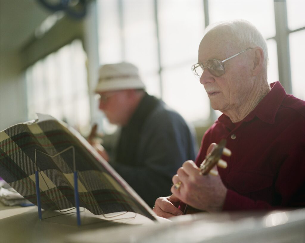 Two elderly men playing ukulele instruments in a senior center.